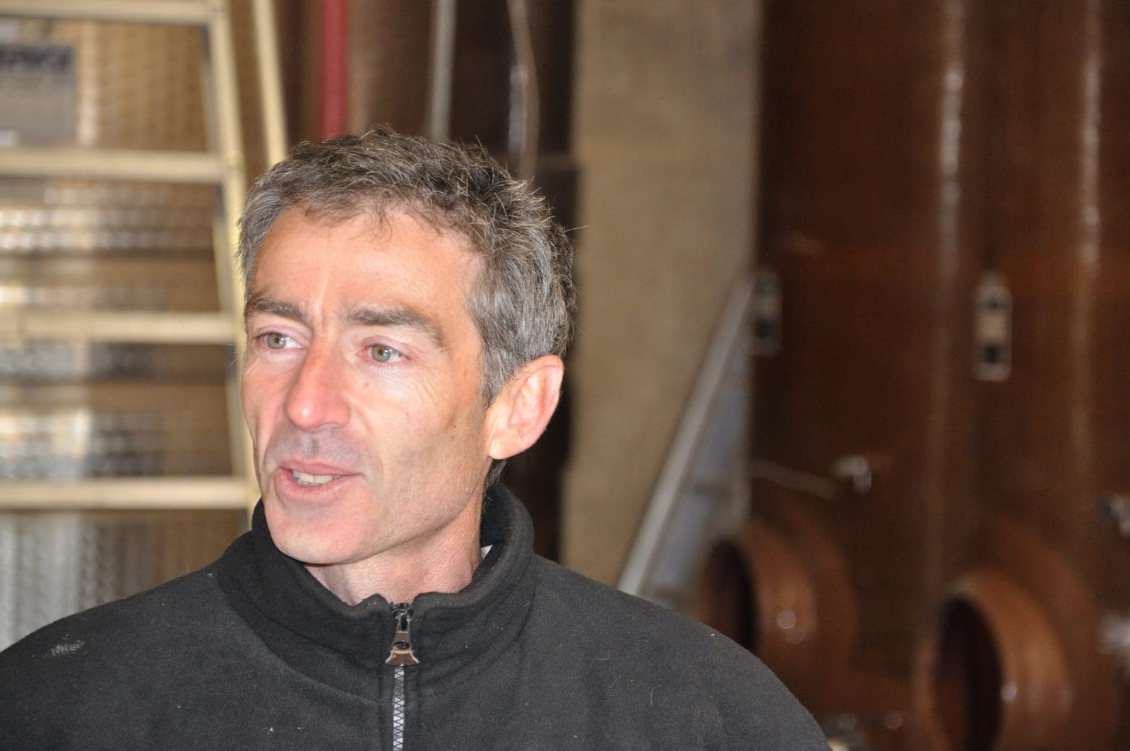 Olivier Jullien speaking in the cellar at Mas Jullien, tanks and foudres behind him.